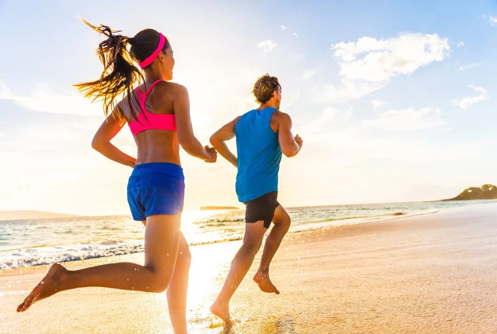 Woman and Man running on the beach in the sunset trying to get in shape for summer